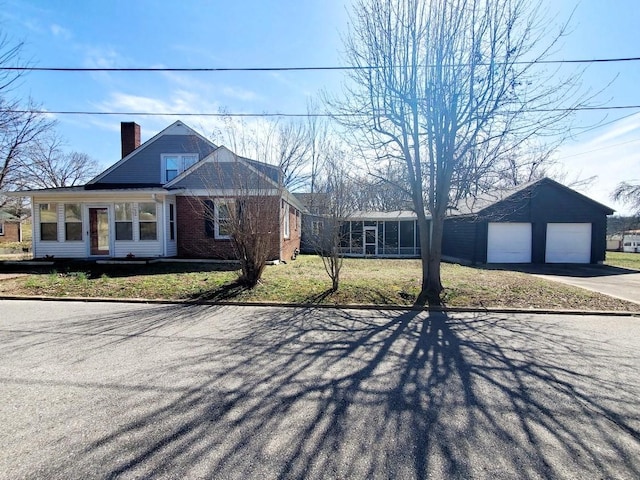 view of front of house featuring brick siding, a garage, a chimney, and an outdoor structure