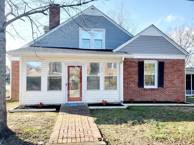 bungalow-style house featuring brick siding, a chimney, and a front yard