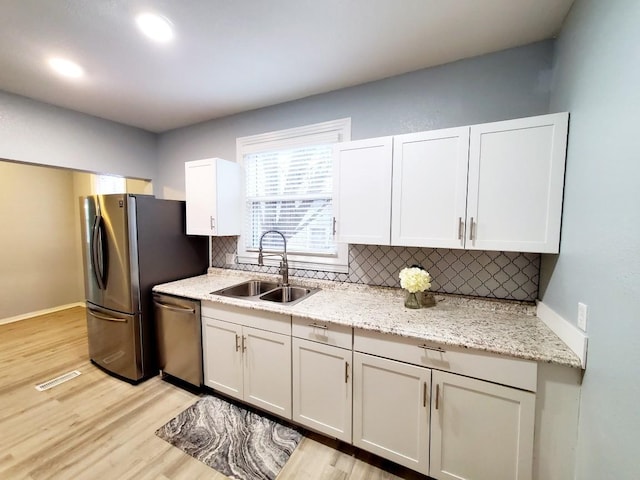 kitchen with decorative backsplash, appliances with stainless steel finishes, light wood-type flooring, and a sink