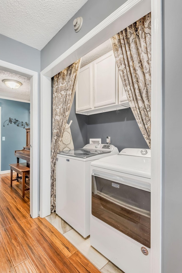 clothes washing area featuring independent washer and dryer, light wood-style flooring, a textured ceiling, cabinet space, and baseboards