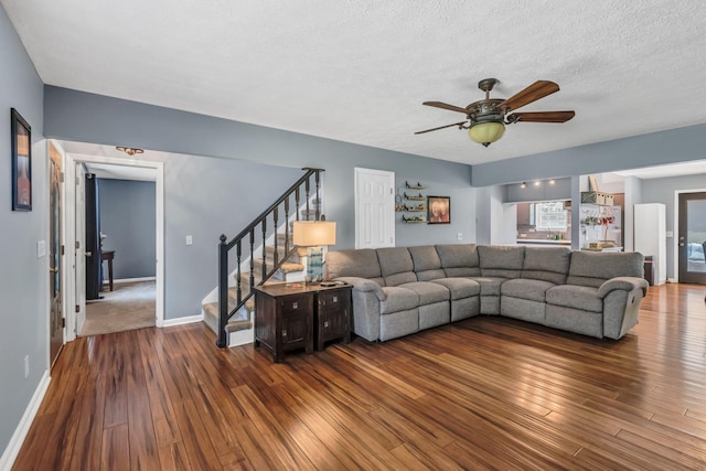 living room featuring stairway, wood finished floors, baseboards, ceiling fan, and a textured ceiling