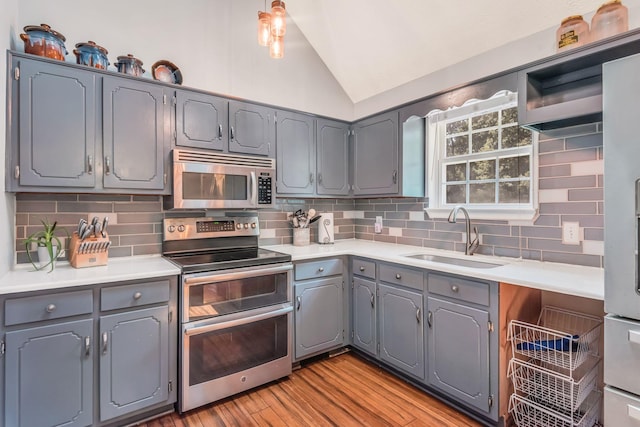 kitchen with lofted ceiling, light wood-style flooring, gray cabinetry, a sink, and appliances with stainless steel finishes