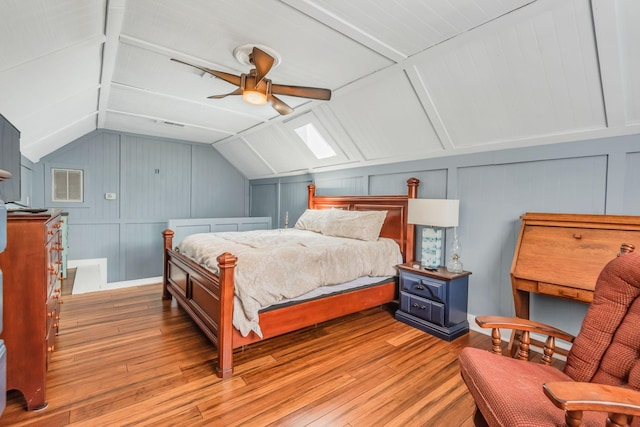 bedroom with visible vents, a ceiling fan, vaulted ceiling with skylight, light wood-style floors, and a decorative wall