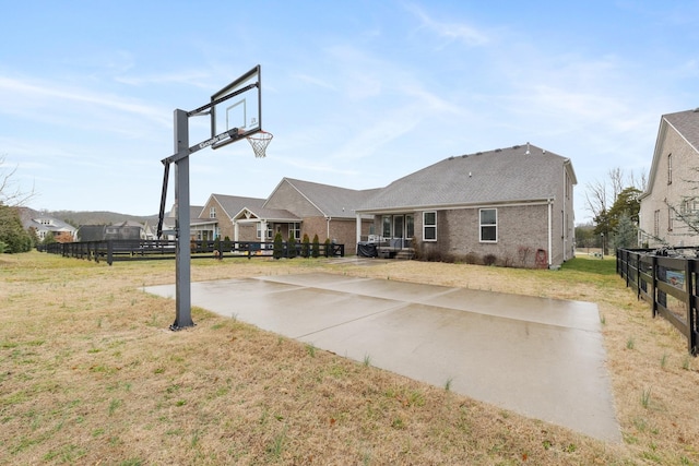 view of sport court featuring basketball hoop, fence, and a lawn