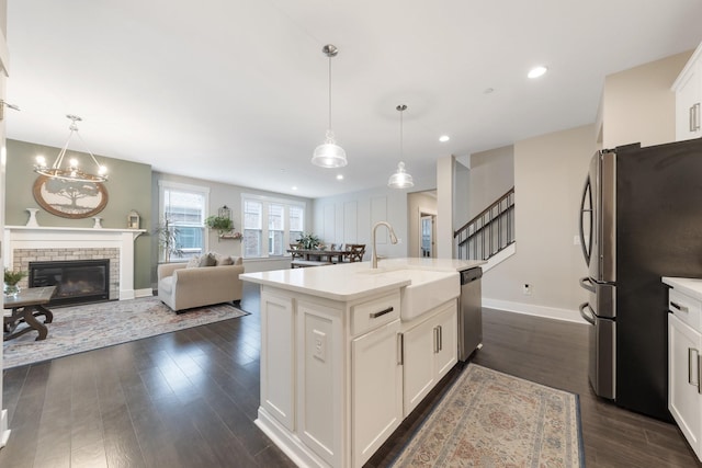 kitchen featuring dark wood-type flooring, a sink, appliances with stainless steel finishes, white cabinets, and a fireplace