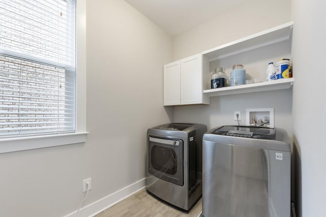 laundry room featuring baseboards, cabinet space, washing machine and dryer, and light wood finished floors