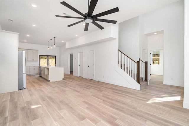 unfurnished living room with a sink, light wood-type flooring, plenty of natural light, and stairs