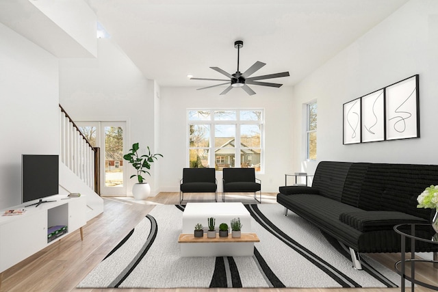 living area featuring light wood-type flooring, ceiling fan, and stairs