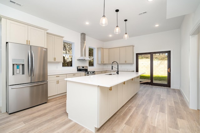 kitchen with wall chimney range hood, light wood finished floors, appliances with stainless steel finishes, and a sink