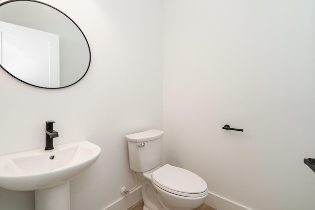 half bathroom with toilet, baseboards, and a sink