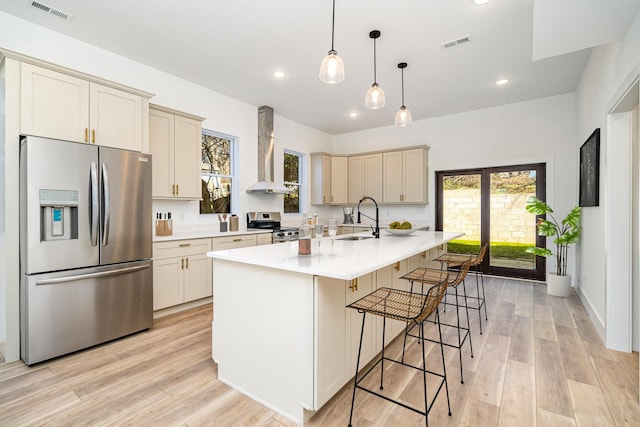 kitchen with a sink, stainless steel appliances, light wood-style floors, and wall chimney range hood