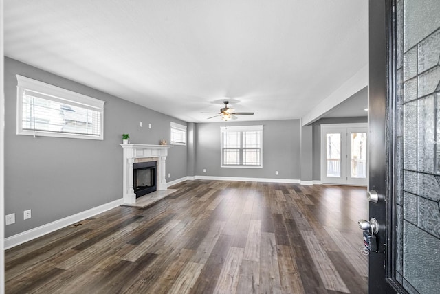 unfurnished living room with baseboards, a ceiling fan, dark wood finished floors, and a fireplace