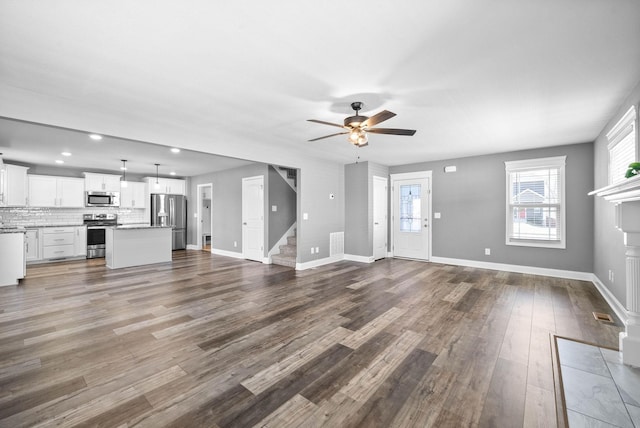 unfurnished living room featuring a fireplace with flush hearth, dark wood-style floors, stairway, baseboards, and ceiling fan