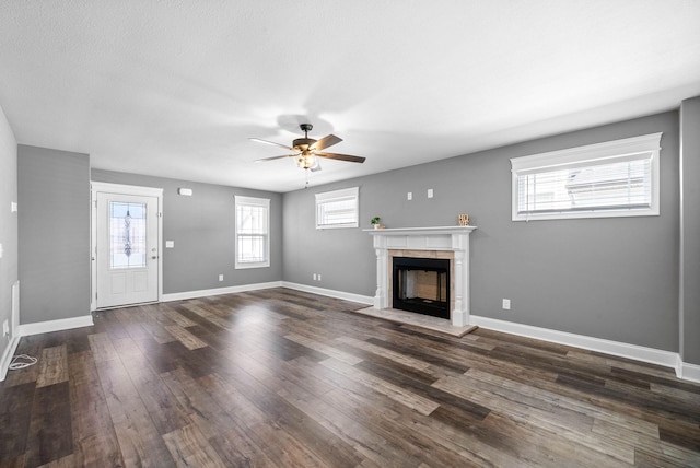 unfurnished living room featuring dark wood finished floors, a tile fireplace, a ceiling fan, and baseboards