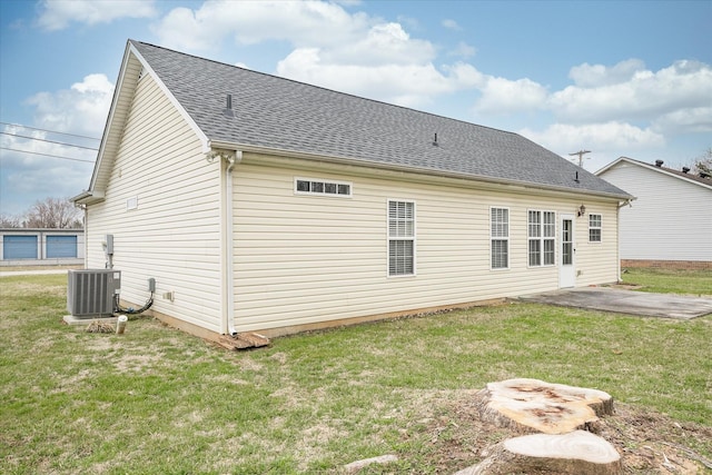 rear view of property featuring a patio area, a lawn, central AC unit, and roof with shingles