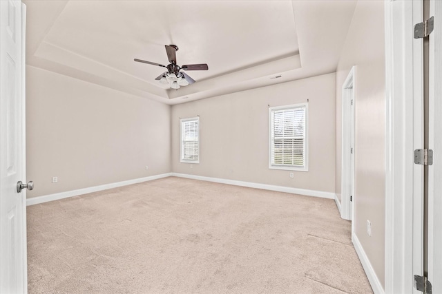 empty room featuring baseboards, a raised ceiling, and light colored carpet