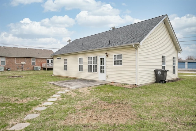 rear view of property featuring a lawn, cooling unit, a shingled roof, and a patio