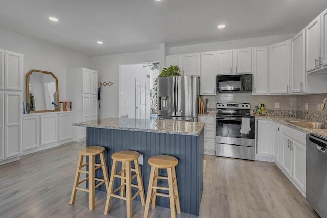 kitchen with a sink, light wood-style floors, appliances with stainless steel finishes, and white cabinetry