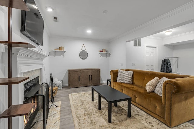 living area featuring visible vents, light wood-style flooring, a fireplace, and ornamental molding