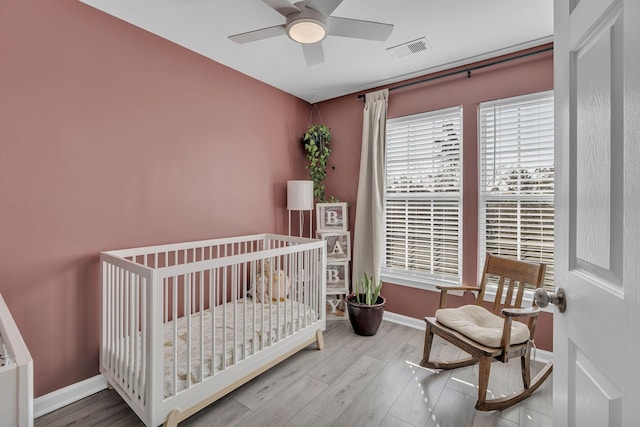 bedroom with visible vents, ceiling fan, baseboards, wood finished floors, and a nursery area