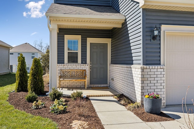 doorway to property featuring brick siding, an attached garage, and a shingled roof