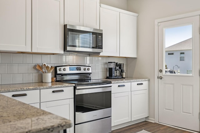 kitchen featuring tasteful backsplash, light stone countertops, appliances with stainless steel finishes, white cabinetry, and dark wood-style flooring