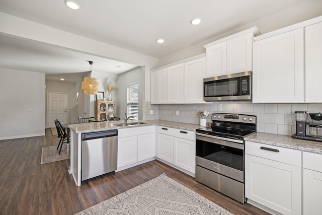 kitchen with decorative backsplash, appliances with stainless steel finishes, a peninsula, white cabinets, and a sink