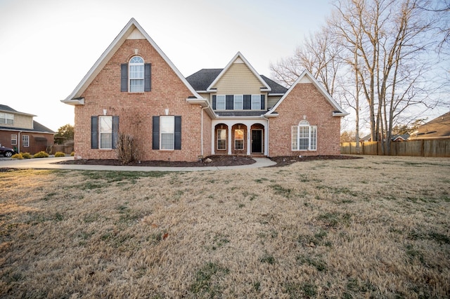 traditional-style house featuring brick siding, a front lawn, and fence