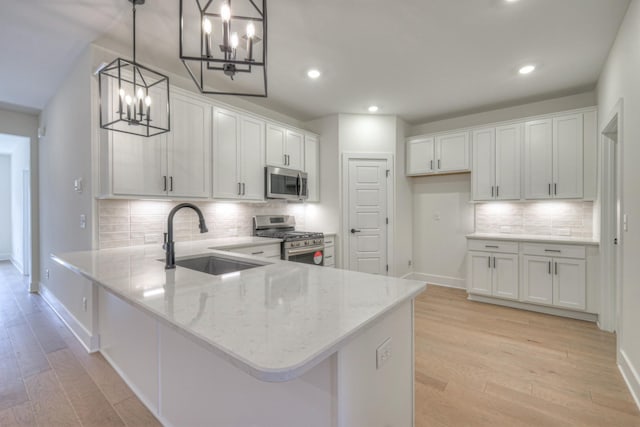 kitchen featuring a peninsula, light wood finished floors, appliances with stainless steel finishes, and a sink