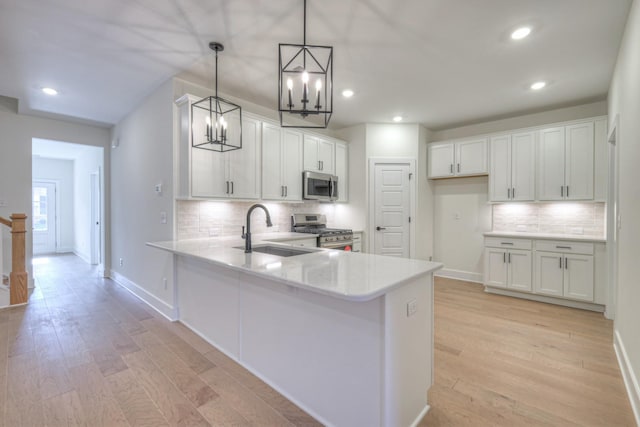 kitchen with baseboards, light wood-type flooring, a peninsula, stainless steel appliances, and a sink