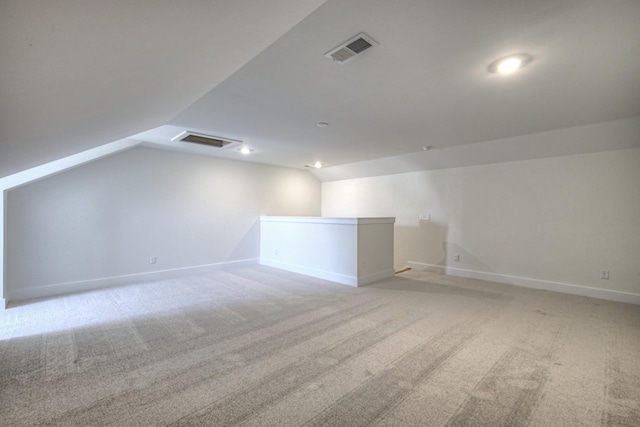 additional living space with visible vents, lofted ceiling, light colored carpet, and attic access