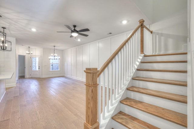 staircase with wood finished floors, visible vents, recessed lighting, a decorative wall, and ceiling fan with notable chandelier