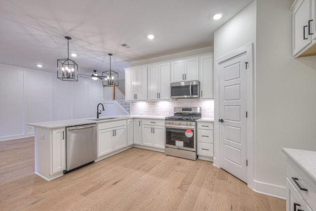 kitchen featuring a peninsula, a sink, stainless steel appliances, light countertops, and backsplash