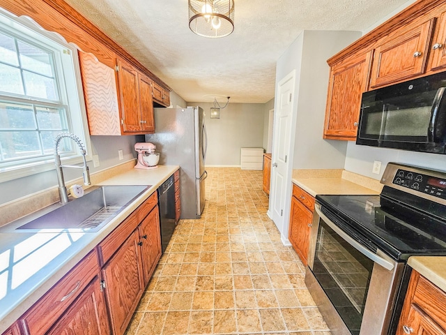 kitchen with brown cabinetry, a sink, black appliances, light countertops, and a textured ceiling