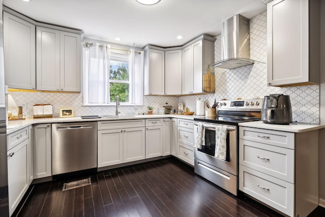 kitchen featuring a sink, wall chimney range hood, light countertops, appliances with stainless steel finishes, and dark wood-style flooring