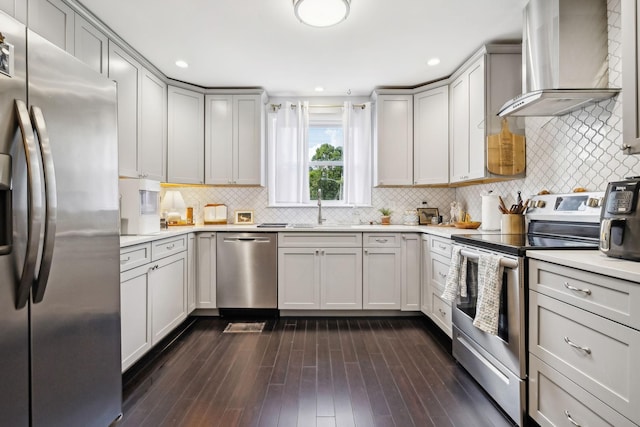 kitchen featuring dark wood-type flooring, wall chimney range hood, light countertops, appliances with stainless steel finishes, and a sink