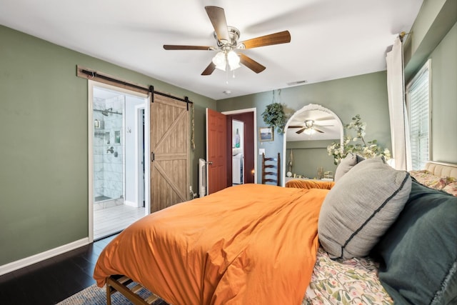 bedroom featuring visible vents, baseboards, a barn door, wood finished floors, and a ceiling fan