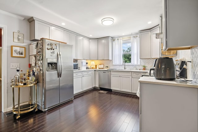 kitchen with a sink, light countertops, decorative backsplash, appliances with stainless steel finishes, and dark wood-style flooring