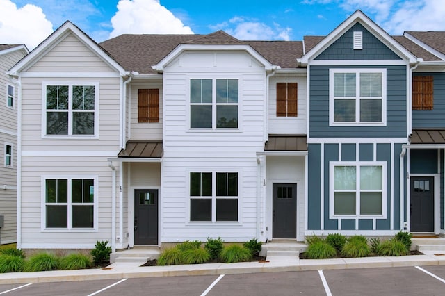 multi unit property featuring a shingled roof, a standing seam roof, and uncovered parking