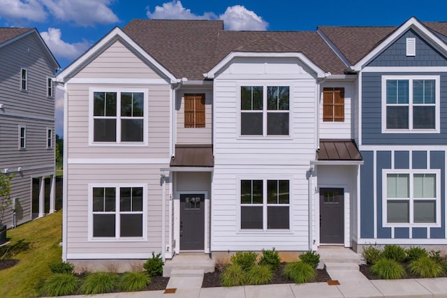 townhome / multi-family property featuring metal roof, a shingled roof, a front yard, and a standing seam roof