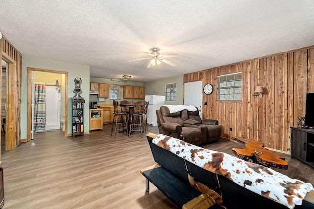 living room with ceiling fan, a textured ceiling, light wood-style flooring, and wooden walls