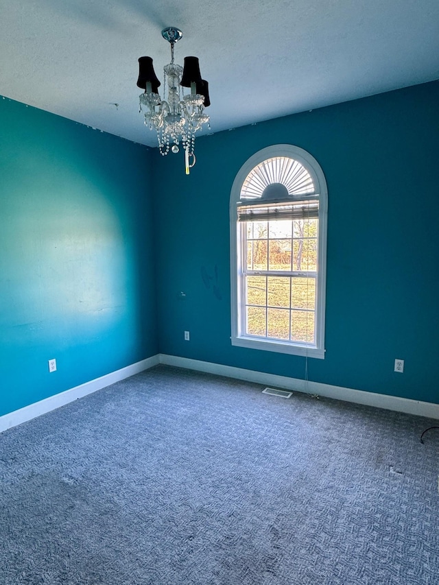 carpeted empty room featuring a notable chandelier, visible vents, a textured ceiling, and baseboards