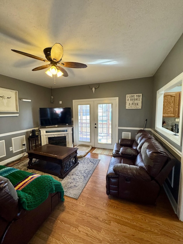 living room featuring french doors, a fireplace, wood finished floors, a textured ceiling, and a ceiling fan