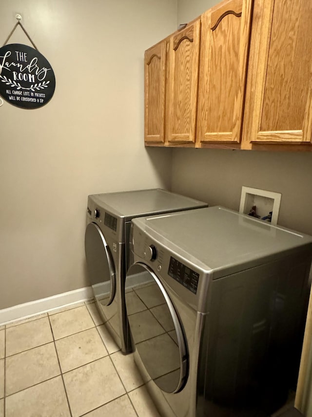 laundry area featuring light tile patterned flooring, washing machine and dryer, cabinet space, and baseboards