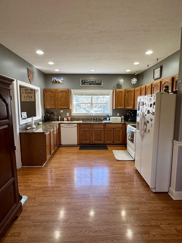 kitchen featuring brown cabinets, a sink, a textured ceiling, wood finished floors, and white appliances