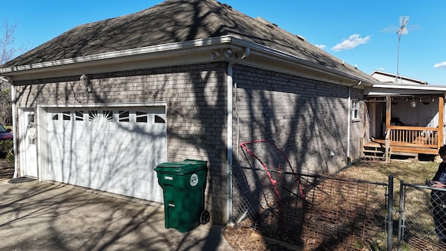 view of side of home with brick siding, a detached garage, fence, a wooden deck, and a gate