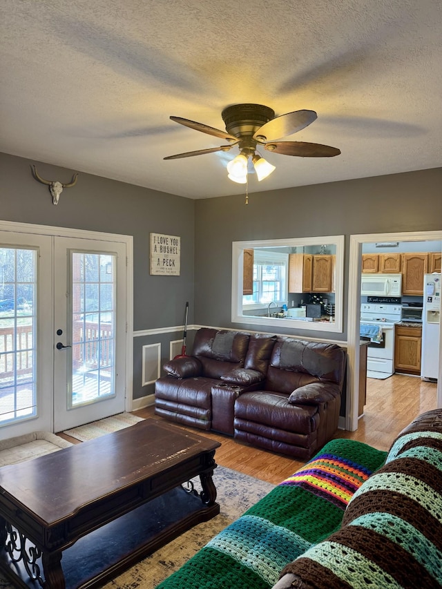 living room with a textured ceiling, light wood finished floors, and ceiling fan