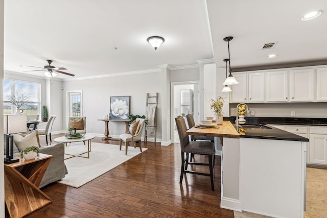 kitchen featuring visible vents, a breakfast bar, a sink, wood finished floors, and white cabinets