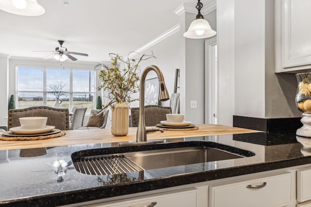 kitchen with crown molding, pendant lighting, dark stone counters, white cabinets, and a sink