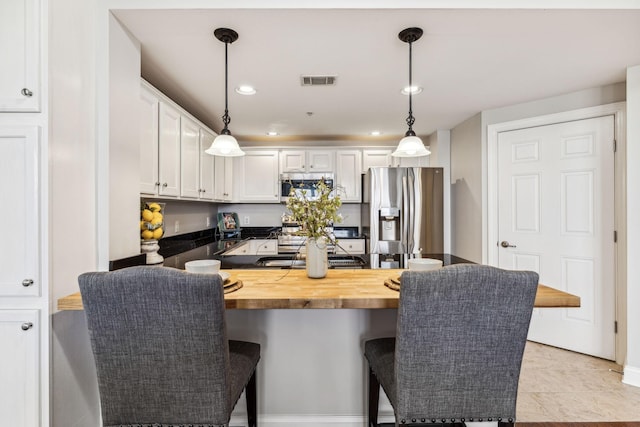 kitchen featuring visible vents, pendant lighting, a breakfast bar area, white cabinets, and stainless steel fridge